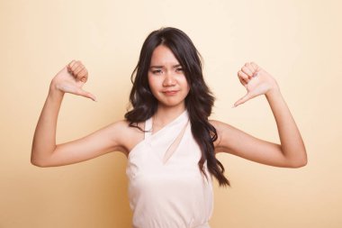 Mutsuz Asyalı kız, bej arka planda iki eliyle baş parmağını kaldırdı.