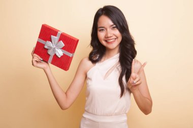 Asyalı kadın bej arka planda hediye kutusuyla zafer işareti gösteriyor.