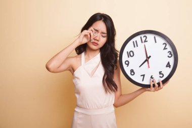 Sabahları bej arka planda saati olan uykulu genç Asyalı kadın.