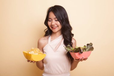 Bej arka planda patates cipsi ve salatalı genç Asyalı kadın.