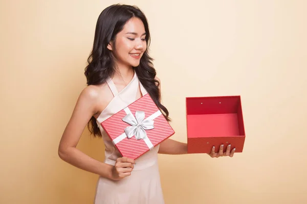 年轻的亚洲女人打开一个米色背景的金色礼品盒 — 图库照片