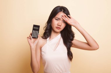 Asyalı kadının bej arka planda hesap makinesiyle başı ağrıyormuş.