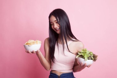 Pembe arka planda patates cipsi ve salatalı genç Asyalı kadın.