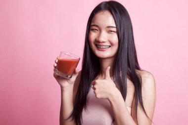 Genç Asyalı kadın pembe arka planda domates suyu ile baş parmağını kaldırdı