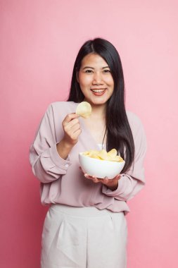 Genç Asyalı kadın pembe arka planda patates cipsi yiyor.
