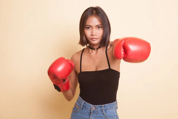 Young Asian woman with red boxing gloves on beige background