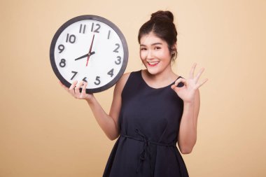 Genç Asyalı kadın bej arka planda bir saatle iyi görünüyor.