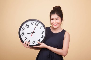 Bej arka planda saati olan genç bir Asyalı kadın.