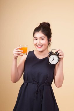 Bej renkli arka plan üzerinde bir saat içki portakal suyuyla Asyalı kadın