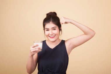 Sağlıklı Asyalı kadın bej arka planda bir bardak süt içiyor.