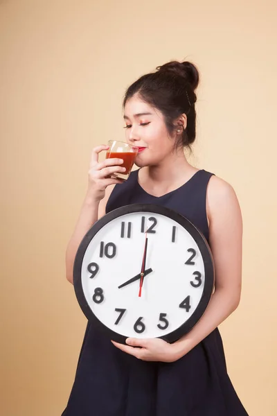 Young Asian woman with tomato juice and clock  on beige background