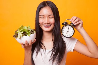 Saat ve parlak sarı zemin üzerine salata ile Genç Asyalı kadın