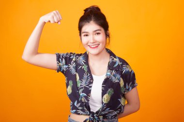 Güzel genç Asyalı kadın flex pazı sarı zemin üzerine tropikal gömlekli