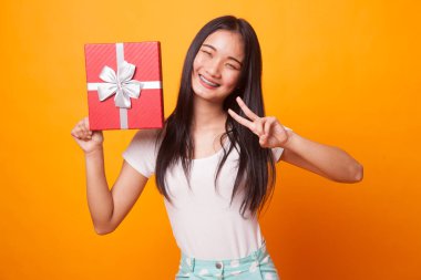 Asyalı kadın parlak sarı arka plan üzerinde zafer işareti bir hediye kutusu ile göster