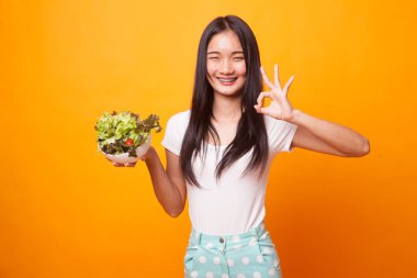Sağlıklı Asyalı kadın parlak sarı zemin üzerine salata ile Tamam göster