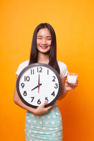 健康亚洲妇女饮用玻璃牛奶保持时钟在明亮的黄色背景 — 图库照片