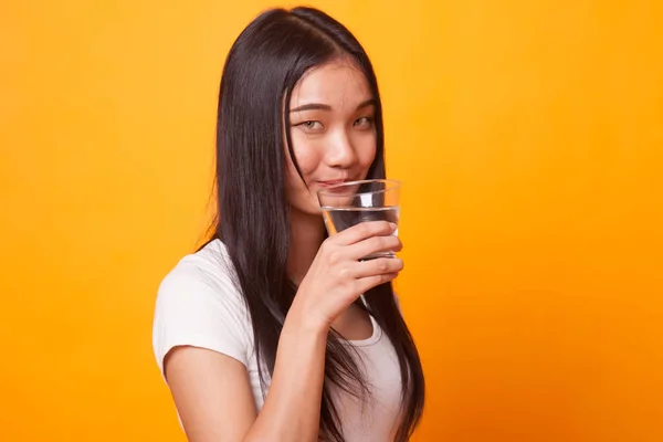 Young Asian woman with a glass of drinking water on bright yellow background