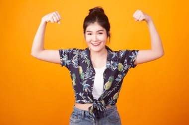 Güzel genç Asyalı kadın flex pazı sarı zemin üzerine tropikal gömlekli