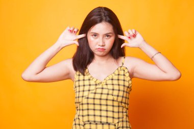 Genç Asyalı kadın her iki kulak Sarı zemin üzerine parmağınızla engellemek