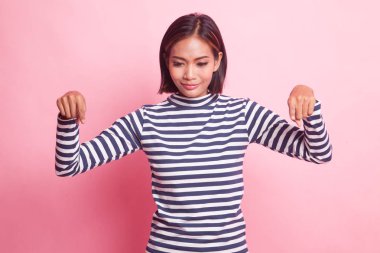 Güzel genç Asyalı kadın pembe arka plandaki boşluğu işaret ediyor.