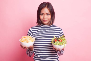 Pembe arka planda patates cipsi ve salatalı genç Asyalı kadın.