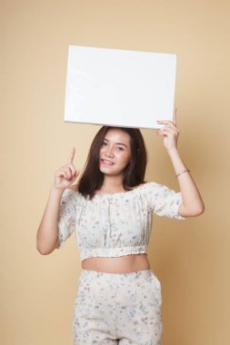 Genç Asyalı kadın bej arka planda boş bir işaret gösteriyor.