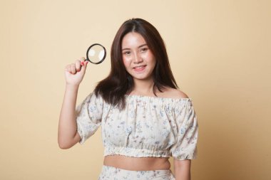 Bej arka planda büyüteçle genç bir Asyalı kadın.