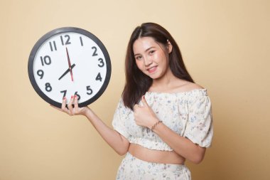 Genç Asyalı kadın bej arka planda bir saatle baş parmağıyla onayladı