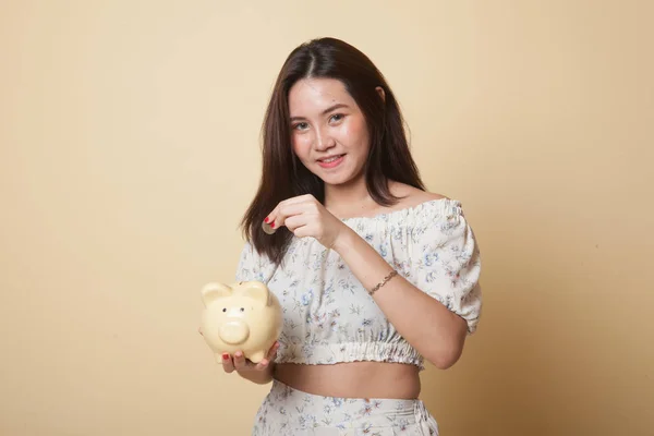 Asian woman with coin and pig coin bank on beige background
