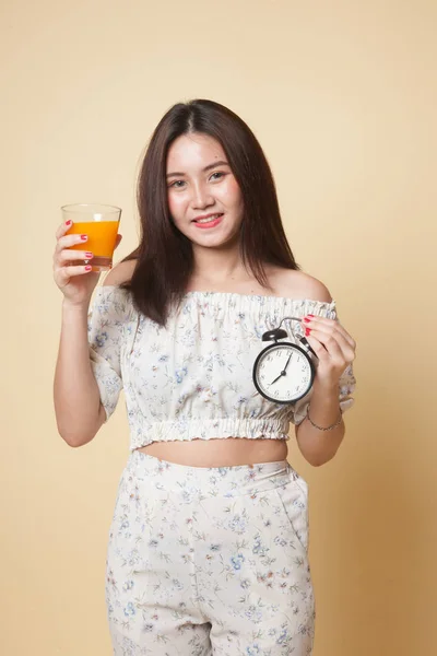 Asian woman with a clock drink orange juice on beige background