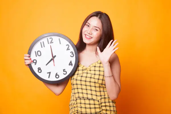 黄色の背景に時計をもつ幸せな若いアジア女性 — ストック写真