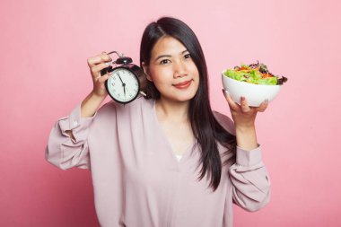 Pembe arka planda saati ve salatası olan genç Asyalı kadın.