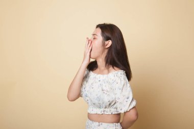 Uykulu genç Asyalı kadın bej arka planda esniyor.