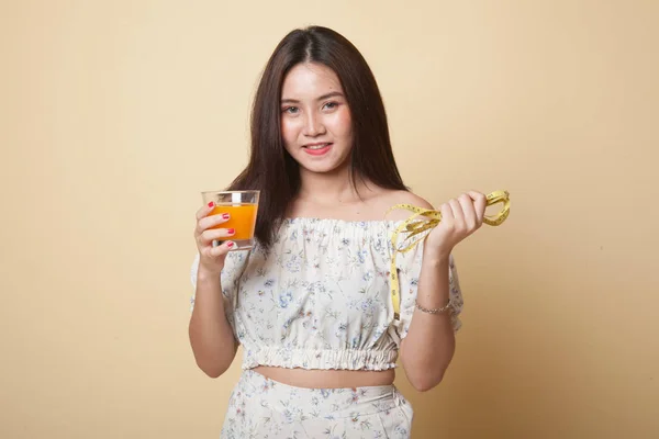 Молодая Азиатка Пьет Апельсиновый Сок Держать Измерительную Ленту Бежевом Фоне — стоковое фото