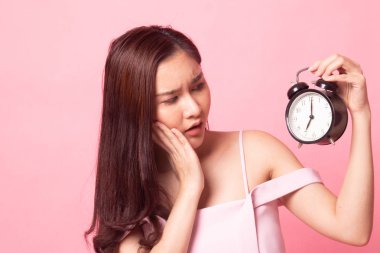 Genç Asyalı kadın pembe arka planda saati olan gülümsüyor.