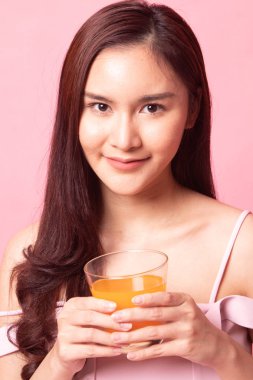 Genç Asyalı kadın pembe arka planda portakal suyu içiyor.
