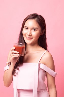 Genç Asyalı kadın pembe arka planda domates suyu içiyor.
