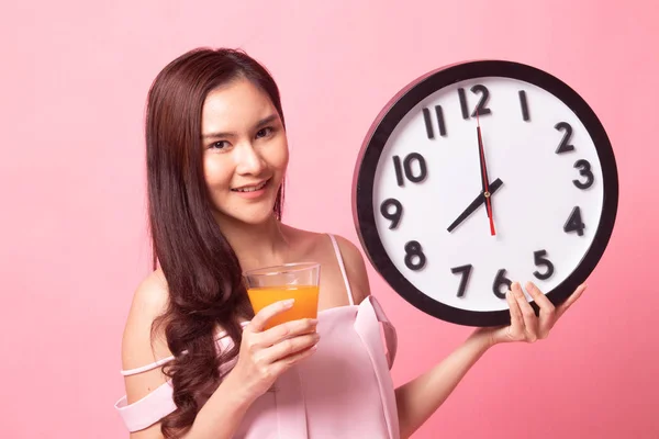 Asian woman with a clock drink orange juice on pink background
