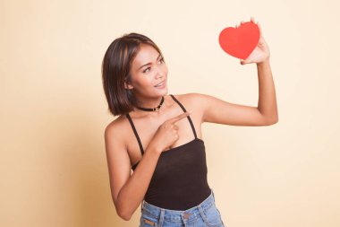 Asyalı kadın bej arka planda kırmızı kalbe işaret ediyor