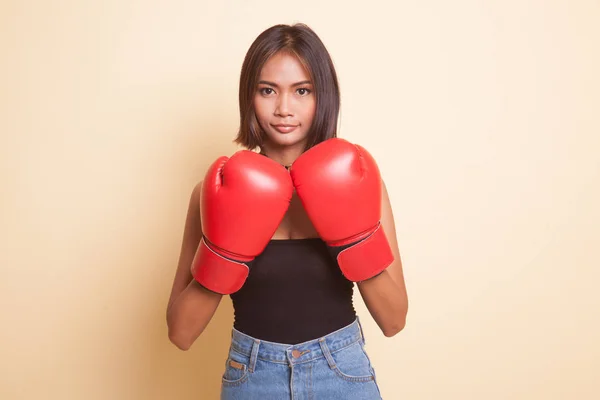 Young Asian woman with red boxing gloves on beige background