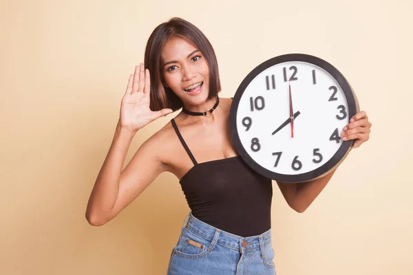 Happy Young Asian woman with a clock on beige background