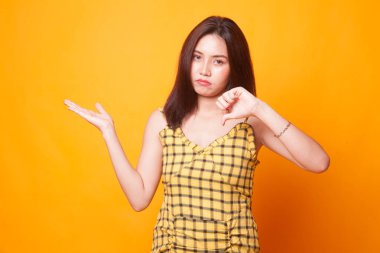 Genç Asyalı kadın göstermek palm el ve başparmak aşağı Sarı zemin üzerine