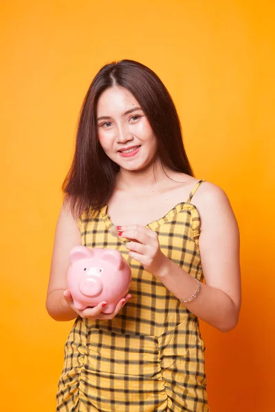 Asian woman with coin and pig coin bank on yellow background