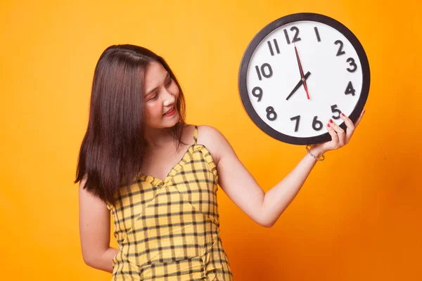 Young Asian woman with a clock on yellow background