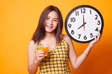 Sarı arka plan üzerinde bir saat içki portakal suyuyla Asyalı kadın