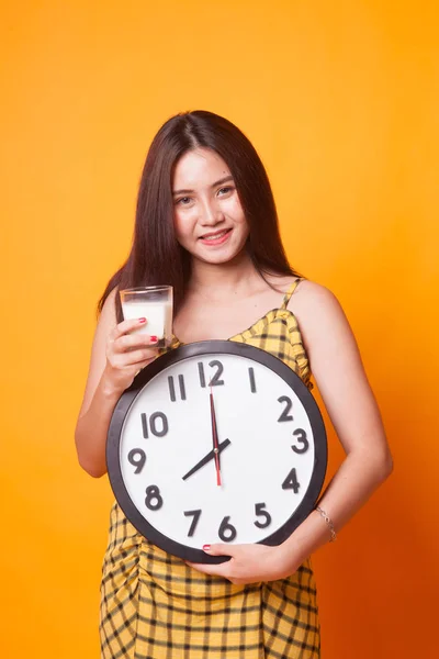 健康的亚洲妇女饮用的牛奶玻璃在黄色背景下举行的时钟 — 图库照片