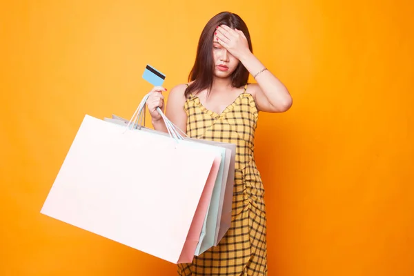 ショッピング バッグと黄色の背景にクレジット カード不幸な若いアジア女性 — ストック写真