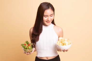 Bej arka planda patates cipsi ve salatalı genç Asyalı kadın..