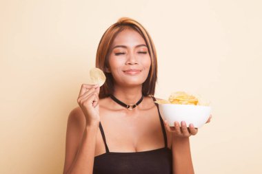 Genç Asyalı kadın bej arka planda patates cipsi yiyor.