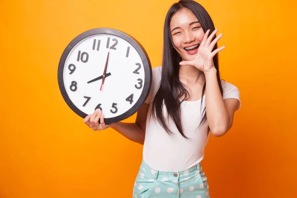 明るい黄色の背景に時計をもつ幸せな若いアジア女性 — ストック写真